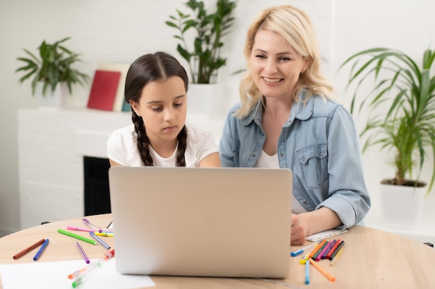 Beautiful young woman and her little cute daughter are using laptop at home. Enjoying spending time together.