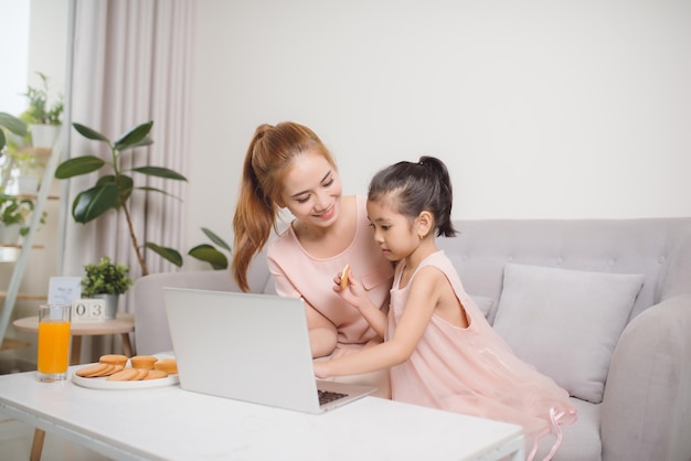 Beautiful young woman and her little cute daughter are using laptop at home