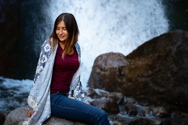 Beautiful young woman hiker sitting near waterfall