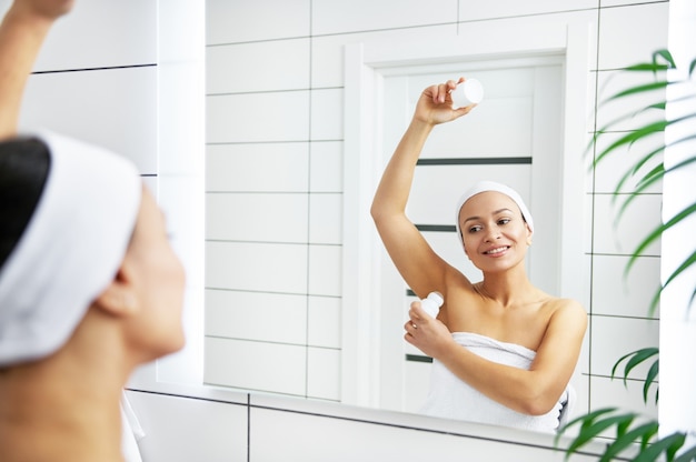 Beautiful young woman holding antiperspirant in hand while rolling it on body