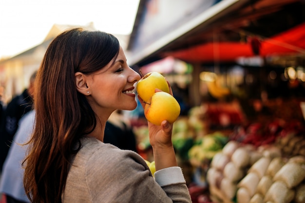 Beautiful young woman holding apple and smelling it 