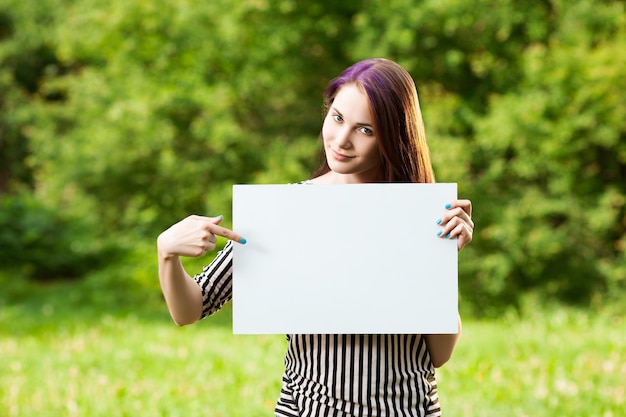 Beautiful young woman holding a blank white board and pointing and it