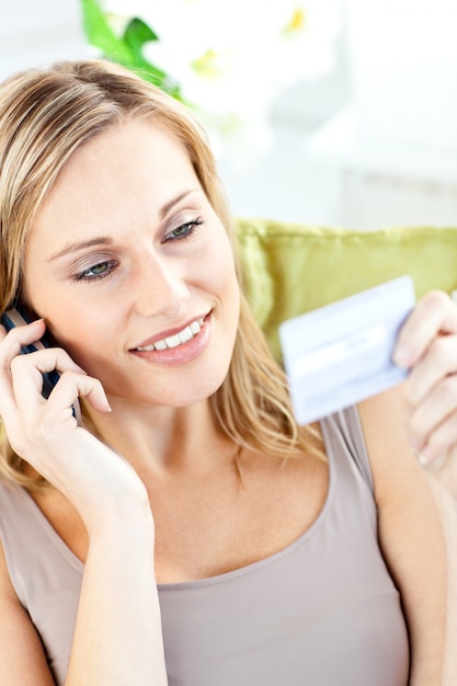 Beautiful young woman holding a card and phoning lying a sofa