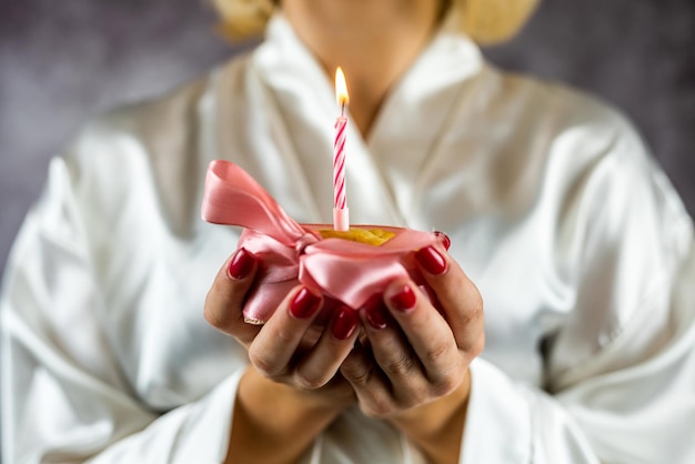 Beautiful young woman holding a cupcake with a colored candle in a silk robe