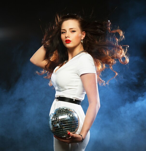 Beautiful young woman holding disco ball at night club