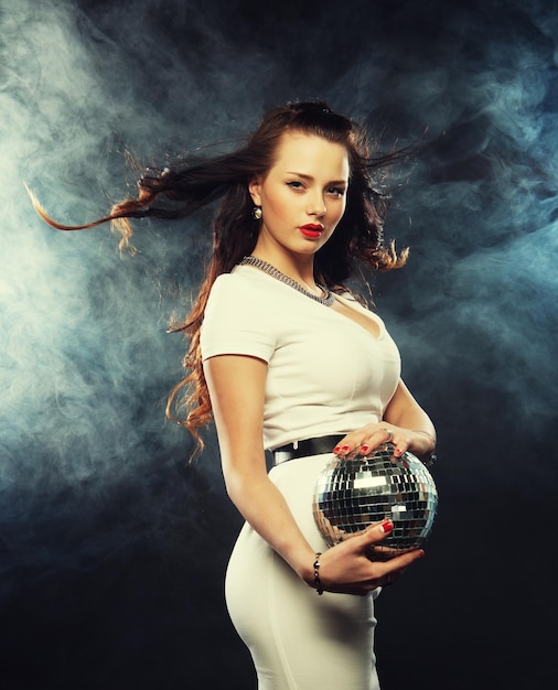 Beautiful young woman holding disco ball at night club