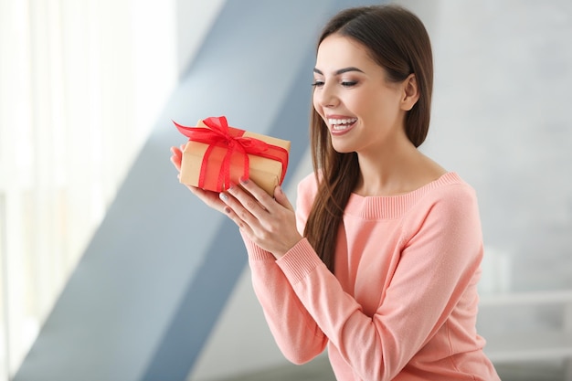 Beautiful young woman holding gift box at home