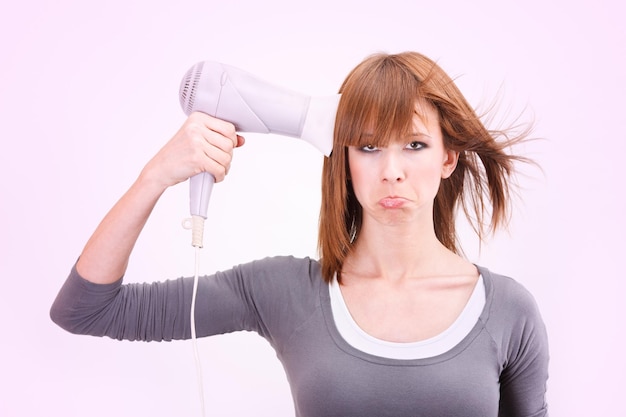 Beautiful young woman holding a hair dryer pointed at head like gun