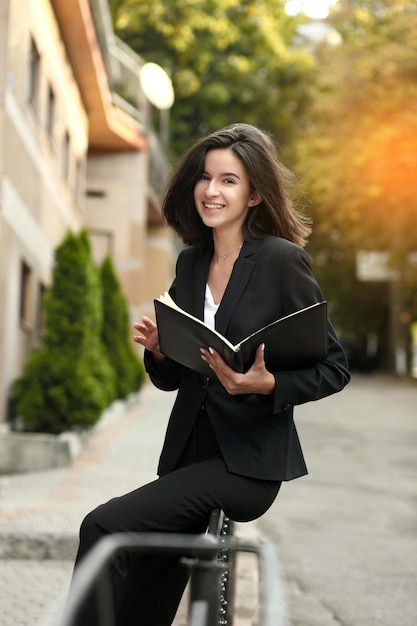 Beautiful young woman holding a notebook in her hands on the street concept of business or education lifestyle