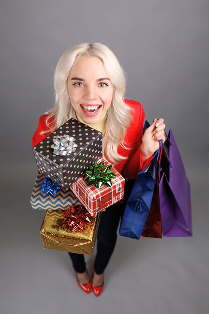 Beautiful young woman holding pile of Christmas presents and shopping bags