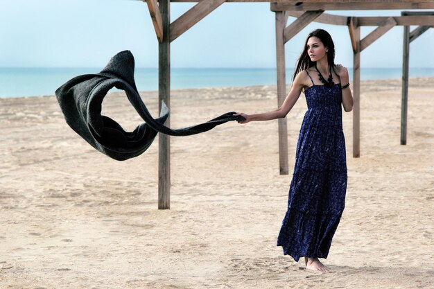 Photo beautiful young woman holding scarf while standing at beach