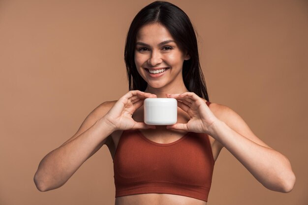 Beautiful young woman holding skincare product and smiling at camera