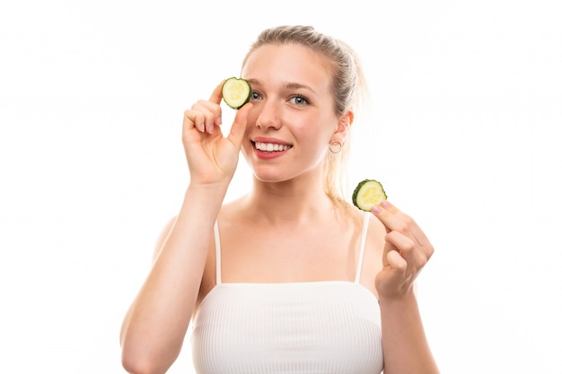 Beautiful young woman holding slices of cucumber over isolated white wall