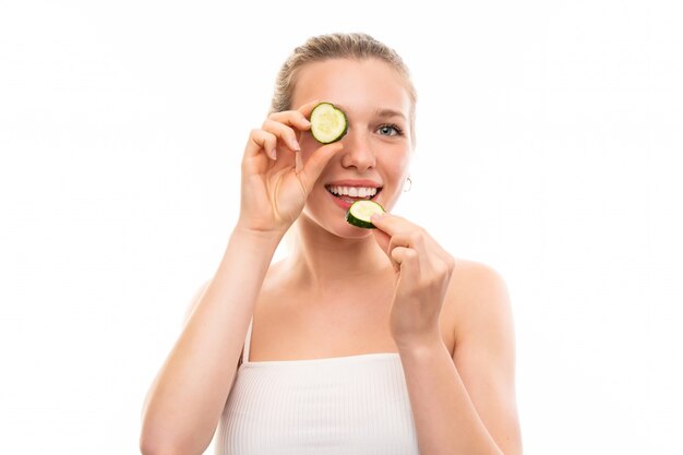 Beautiful young woman holding slices of cucumber over isolated white