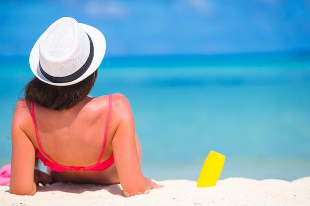 Beautiful young woman holding a suncream lying on tropical beach