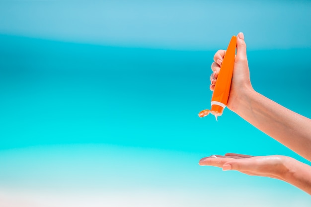 Beautiful young woman holding a suncream lying on tropical beach