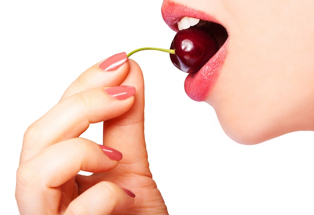 beautiful young woman holds a cherry in her hand and puts it in her open mouth close-up