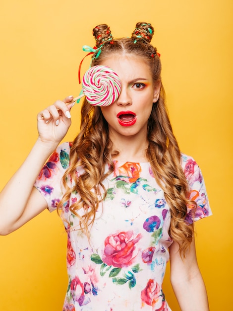 Beautiful young woman holds in hand candy, emotion of indignation on her face. Stylish girl in summer colorful dress.