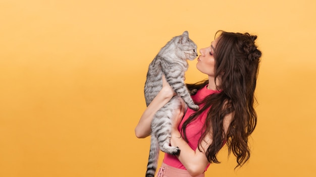 A beautiful young woman holds a tabby cat in her arms on orange background