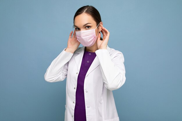 Beautiful young woman holds and wears a white medical mask to protect yourself from corona virus