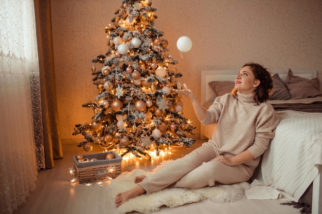 クリスマスツリーの近くの寝室で自宅で美しい若い女性。