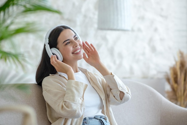 Beautiful young woman at home relaxing listening to music from white headphones sitting on the sofa