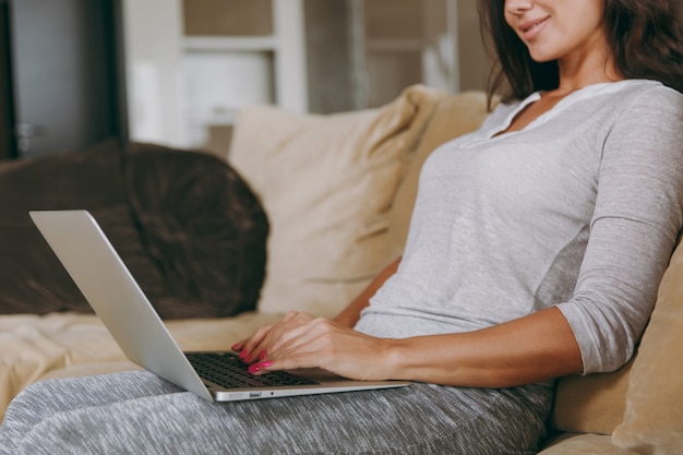 The beautiful young woman at home sitting on the sofa, relaxing in her living room and working with laptop