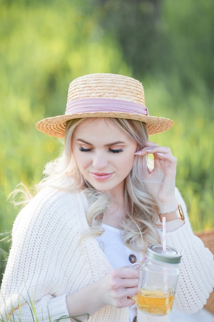写真 籐の帽子をかぶった美しい若い女性は、咲く庭でピクニックで休んでいます。白い花。春。幸福。