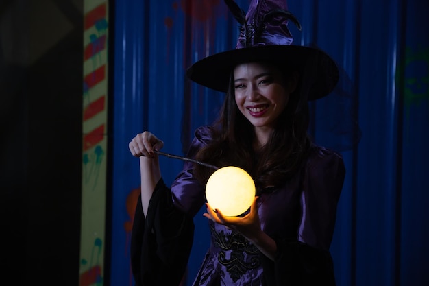 写真 魔女の帽子と衣装で美しい若い女性。暗い夜に魔法のライトでハロウィーンの魔女。ハロウィーンパーティー。