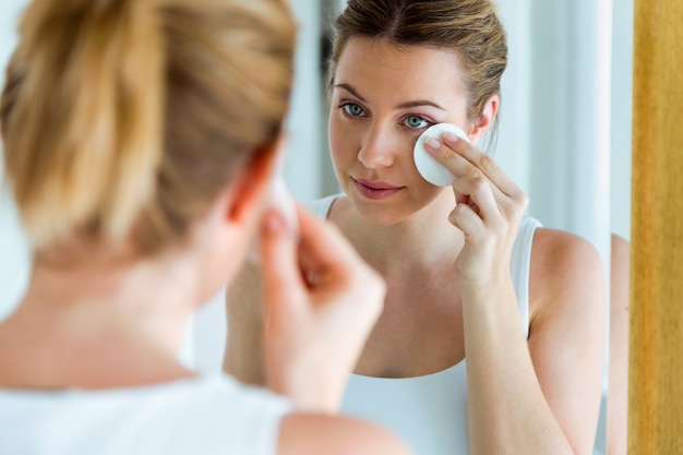 Beautiful young woman is cleaning her face while looking in the mirror in the bathroom.