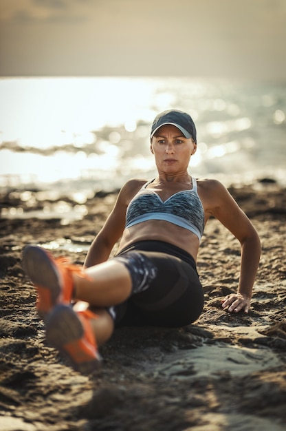 Красивая молодая женщина занимается перекрестными тренировками на морском пляже в летний солнечный день на закате.
