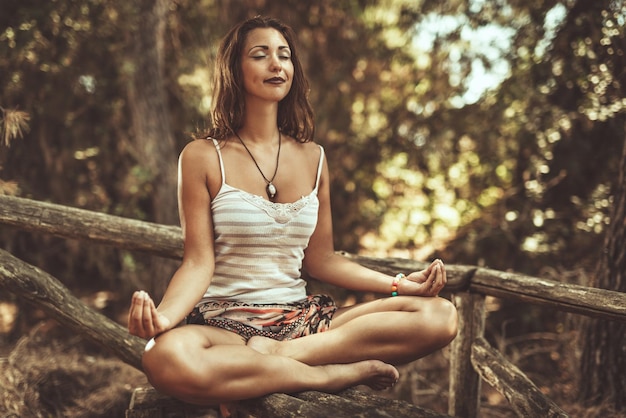 Красивая молодая женщина занимается йогой и медитирует в сосновом лесу летом.