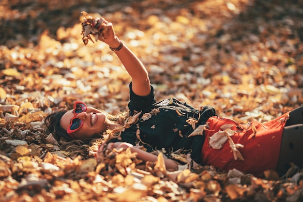 Фото Красивая молодая женщина наслаждается цветами осеннего солнечного леса. она лежит на золотисто-желтых листьях и веселится.