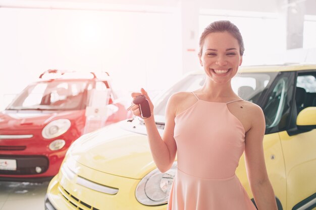 Beautiful young woman is holding a key in car dealership