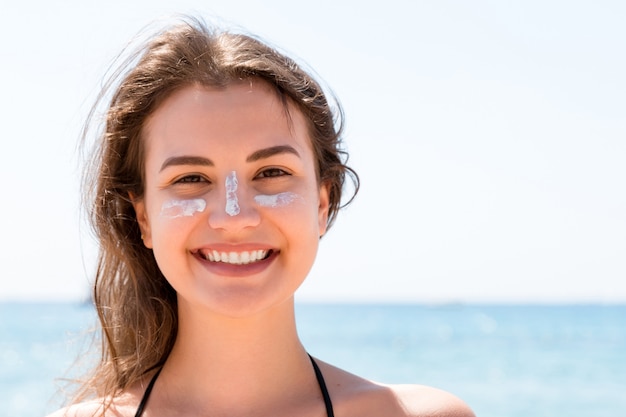 Foto bella giovane donna sta proponendo alla telecamera con crema solare sul viso sopra il mare.