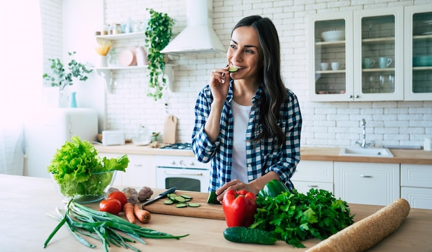 美しい若い女性がキッチンで野菜サラダを準備しています。健康食品。ビーガンサラダ。ダイエット。ダイエットの概念。健康的な生活様式。家庭での料理。食べ物を用意します。テーブルの上の材料を切る