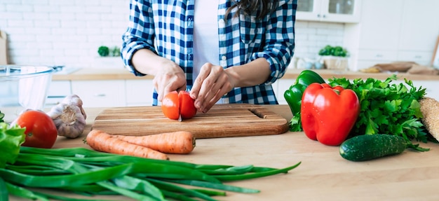 美しい若い女性がキッチンで野菜サラダを準備しています。健康食品。ビーガンサラダ。ダイエット。ダイエットの概念。健康的な生活様式。家庭での料理。食べ物を用意します。テーブルの上の材料を切る