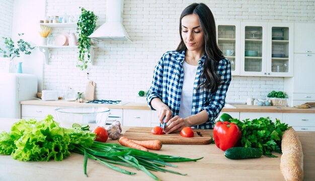 美しい若い女性がキッチンで野菜サラダを準備しています。健康食品。ビーガンサラダ。ダイエット。ダイエットの概念。健康的な生活様式。家庭での料理。食べ物を用意します。テーブルの上の材料を切る