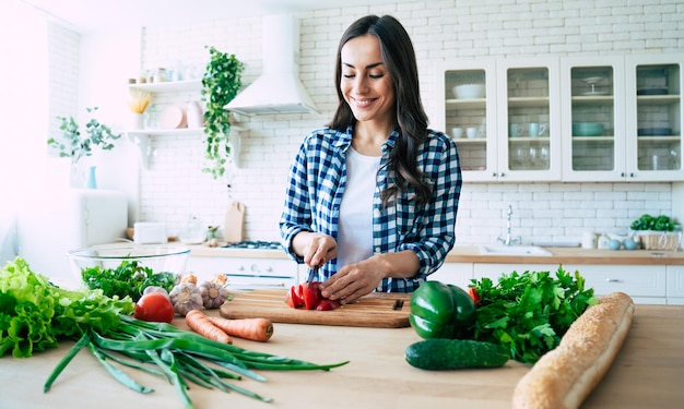 Beautiful young woman is preparing vegetable salad in the kitchen. Healthy Food. Vegan Salad. Diet. Dieting Concept. Healthy Lifestyle. Cooking At Home. Prepare Food. Cutting ingredients on table