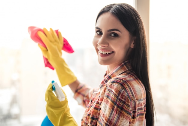 Beautiful young woman is smiling while cleaning window.