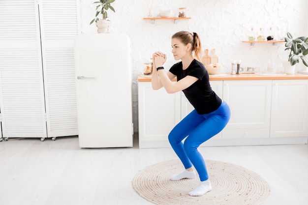 Beautiful young woman is standing on blue mat doing squats exercise