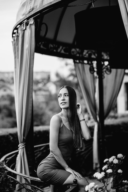 A beautiful young woman is standing on the veranda of a beautiful house. Black and white.