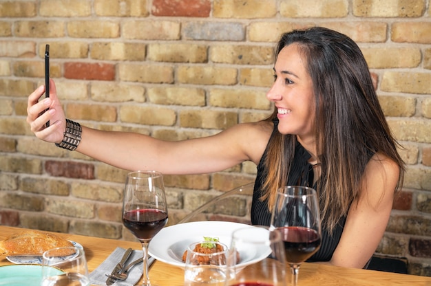 아름 다운 젊은 여자는 레스토랑에서 식사하는 동안 셀카 사진을 찍고있다.
