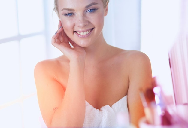 Beautiful young woman is touching her face and smiling while looking at the mirror