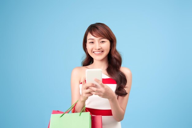 Красивая молодая женщина использует смартфон для покупок в Интернете, изолированных на синем фоне студии