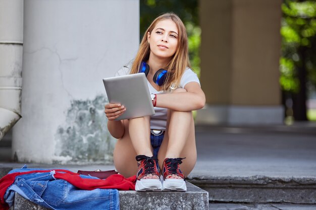 美しい若い女性が公園でタブレットコンピューターを使用しています。