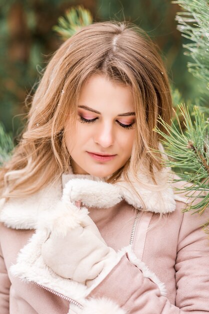 Beautiful young woman in jeans and pink jacket in winter forest