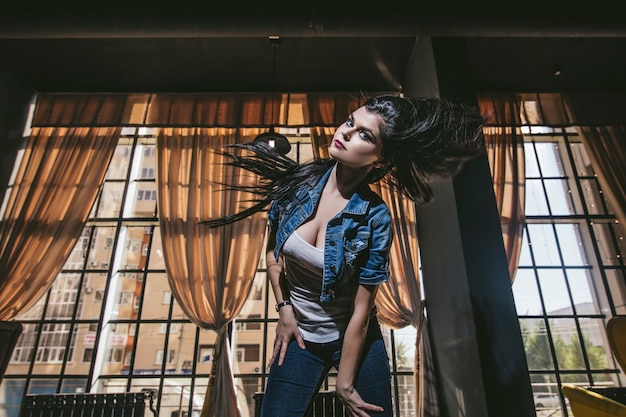 Photo beautiful young woman in jeans and sneakers in front of large windows in an urban loft