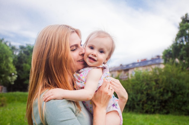 The beautiful young woman kisses a toddler girl in the garden The blonde woman holding a funny baby in her arms