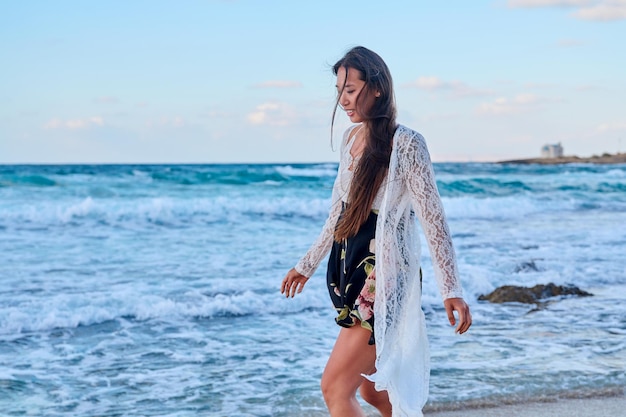 Beautiful young woman in a lace dress walking along the beach copy space